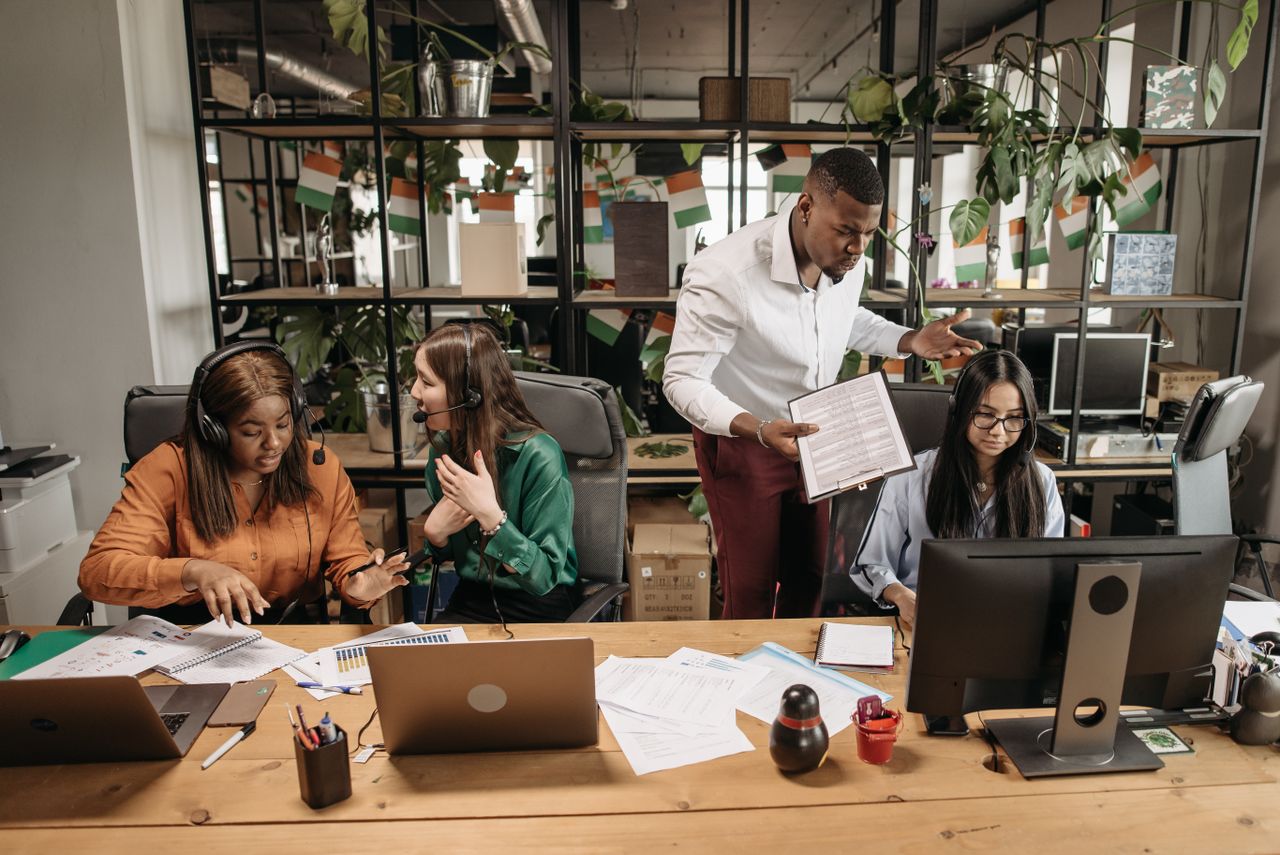 A diverse team of call center agents in a lively office setting, collaborating on tasks and discussing reports.